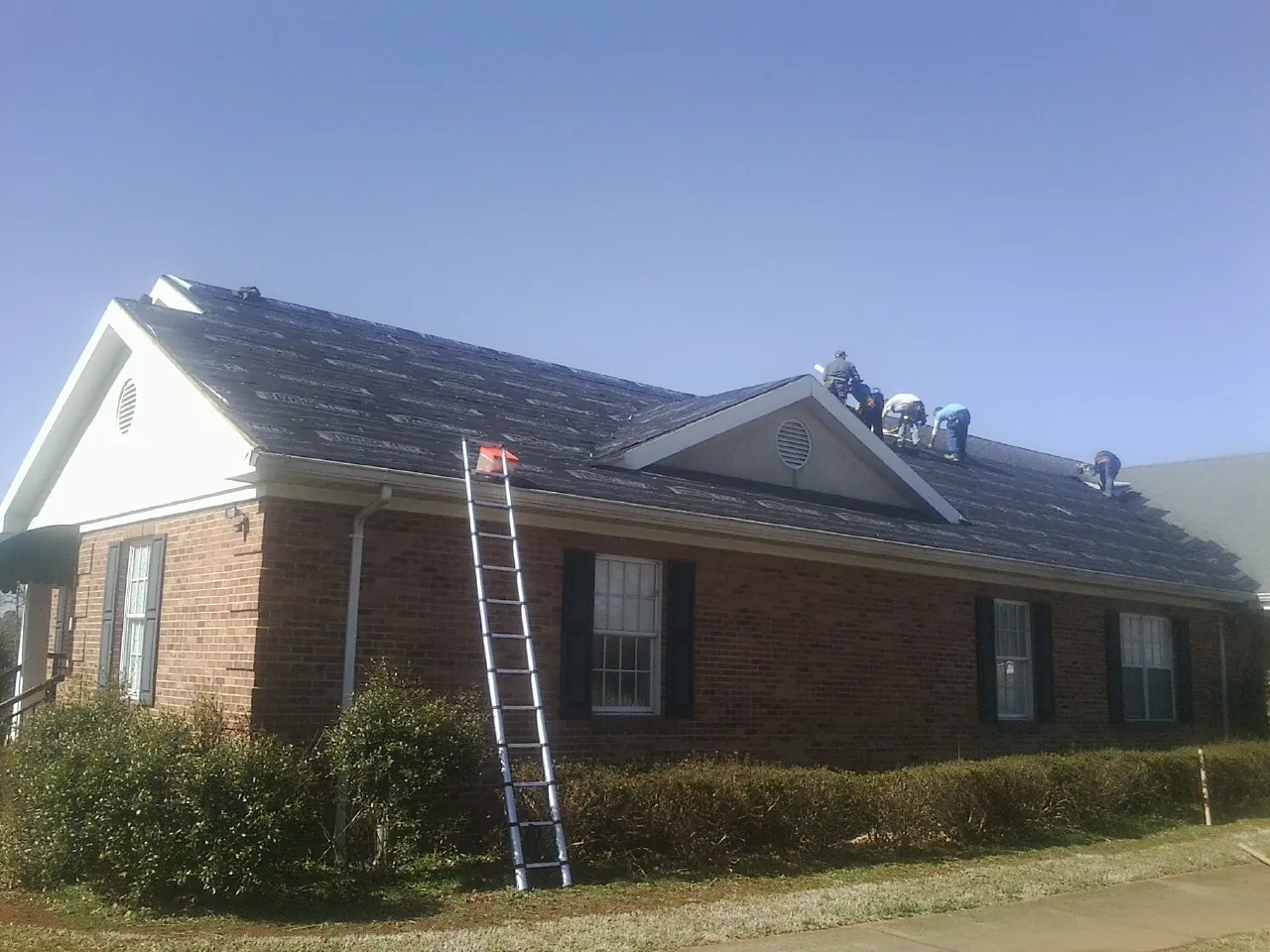 Crew tearing shingles off a brick ranch roof with a ladder set — Metal Roof Repair work by our crew in Hillsboro
